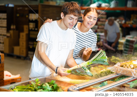 Young woman and young guy choosing leeks in grocery store Young woman and young guy choosing leeks in grocery store 140554035
