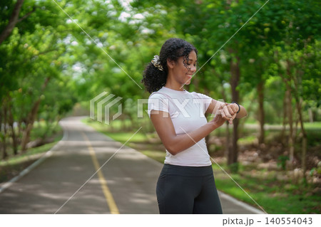 Smiling Black woman checking smartwatch during outdoor fitness exercise in green park wellness healthy lifestyle Smiling Black woman checking smartwatch during outdoor fitness exercise in green park wellness healthy lifestyle 140554043
