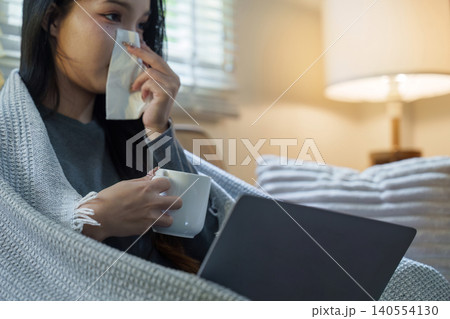 Sick Asian woman blowing nose while using laptop at home Sick Asian woman blowing nose while using laptop at home 140554130