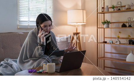 Asian woman feeling unwell talking on phone with laptop for telehealth Asian woman feeling unwell talking on phone with laptop for telehealth 140554142