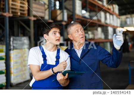 Guy check papers invoices together with mature employee and revise availability of goods in stock Guy check papers invoices together with mature employee and revise availability of goods in stock 140554143