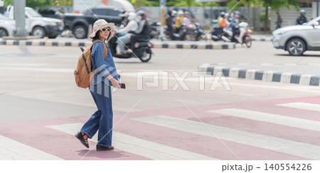 Asian woman tourist crossing urban street with backpack for city exploration and summer travel Asian woman tourist crossing urban street with backpack for city exploration and summer travel 140554226