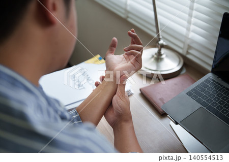 Asian man experiencing wrist pain while working at home office Asian man experiencing wrist pain while working at home office 140554513