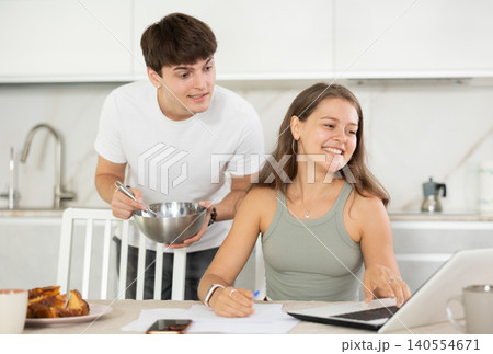 Happy young woman using laptop in the kitchen while communicating with her boyfriend Happy young woman using laptop in the kitchen while communicating with her boyfriend 140554671