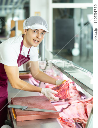 Positive young salesman demonstrating piece of meat in butcher shop Positive young salesman demonstrating piece of meat in butcher shop 140554759