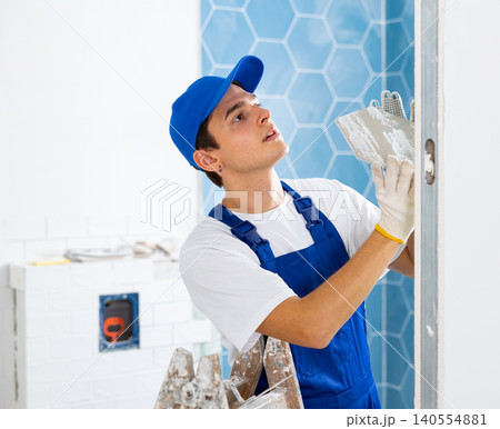 Young contractor laying tiles on walls during indoor renovation works 140554881