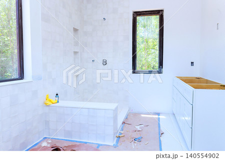 Construction workers are installing bathtub cabinets in new bathroom while sunlight shines through windows. Construction workers are installing bathtub cabinets in new bathroom while sunlight shines through windows. 140554902
