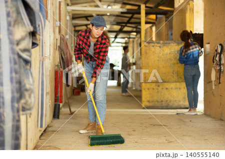 Girl cleans the floor of a stable with fetlock Girl cleans the floor of a stable with fetlock 140555140