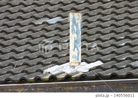 An ageing and weathered air vent pipe on an old and deteriorating tiled roof 140556011