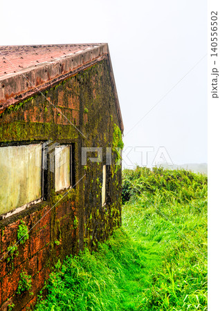 An old concrete building covered in vibrant green moss stands on the foggy slopes of Mount Pelee in Martinique, Caribbean France An old concrete building covered in vibrant green moss stands on the foggy slopes of Mount Pelee in Martinique, Caribbean France 140556502