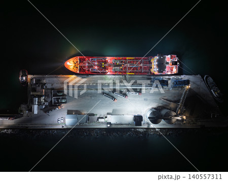 Top down View of Port Tanker and Grain Silos. High oleic sunflower oil is loaded from tanker trucks onto a tanker ship. Deep night photo Top down View of Port Tanker and Grain Silos. High oleic sunflower oil is loaded from tanker trucks onto a tanker ship. Deep night photo 140557311