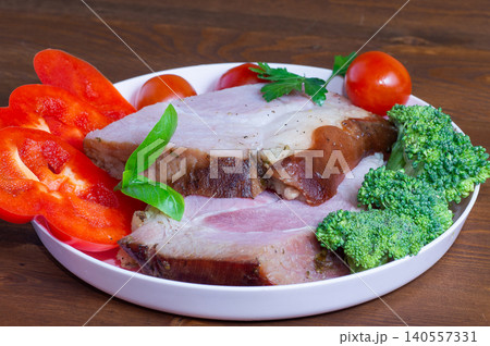 Baked HAM steaks lie on green lettuce leaves, cherry tomatoes and broccoli. Baked HAM steaks lie on green lettuce leaves, cherry tomatoes and broccoli. 140557331