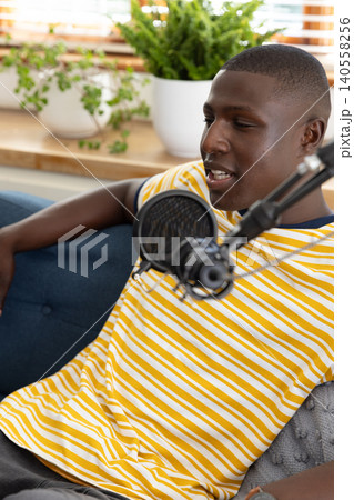 African american adult male sitting on couch at home studio speaking into condenser microphone African american adult male sitting on couch at home studio speaking into condenser microphone 140558256