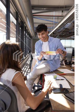 Coworkers presenting color swatch card while collaborating at studio desk with sticky notes 140558306