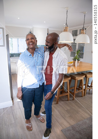 Senior African American mother and son hugging in modern kitchen with wooden island and fruit bowl Senior African American mother and son hugging in modern kitchen with wooden island and fruit bowl 140558315