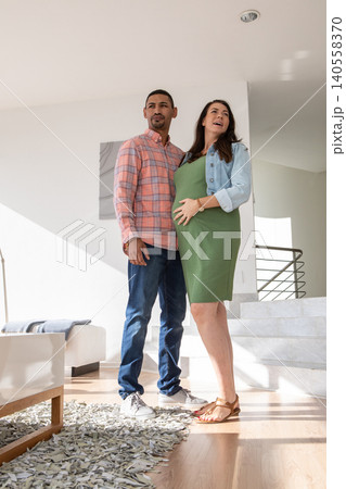Diverse couple standing in hallway with pregnant woman wearing green dress near staircase and art Diverse couple standing in hallway with pregnant woman wearing green dress near staircase and art 140558370
