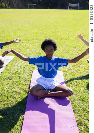 African american teen meditating cross-legged on mat on sports field near soccer goalposts African american teen meditating cross-legged on mat on sports field near soccer goalposts 140558422