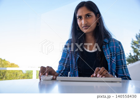 Indian woman typing on white keyboard and using wireless mouse at balcony desk Indian woman typing on white keyboard and using wireless mouse at balcony desk 140558430