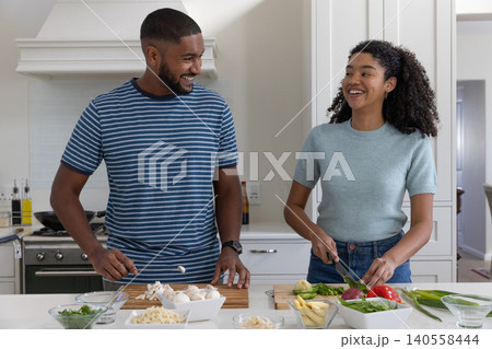 Diverse couple slicing asparagus and bell peppers on kitchen island cutting boards 140558444