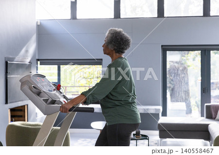 Senior african american woman walking briskly on treadmill in living room Senior african american woman walking briskly on treadmill in living room 140558467