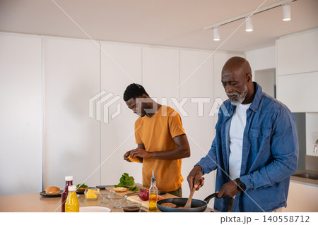 African american senior father stirring pan, son slicing vegetables on board at kitchen island African american senior father stirring pan, son slicing vegetables on board at kitchen island 140558712