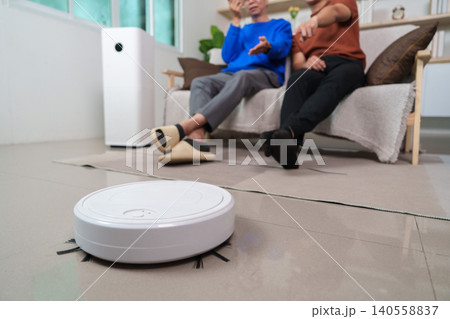 Robot vacuum cleaner working on floor with blurred Asian men in background 140558837