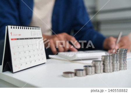 Person calculating finance budget savings with calendar and coins on desk Person calculating finance budget savings with calendar and coins on desk 140558882