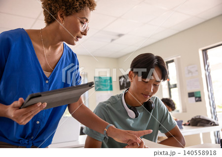 Female teacher and asian teen student wearing headphones holding tablet pointing at papers Female teacher and asian teen student wearing headphones holding tablet pointing at papers 140558918