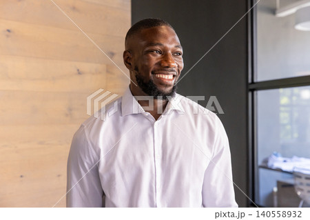 African american man smiling while standing in office by wood-paneled wall, glass partition African american man smiling while standing in office by wood-paneled wall, glass partition 140558932