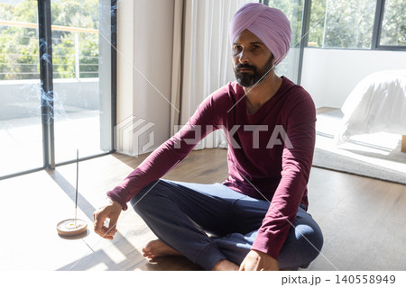 Indian man meditating cross-legged on hardwood bedroom floor near burning incense holder 140558949