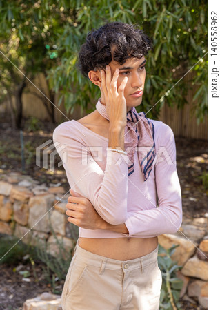 Man with arms crossed and hand to face in backyard by stone wall wearing scarf, bracelet Man with arms crossed and hand to face in backyard by stone wall wearing scarf, bracelet 140558962