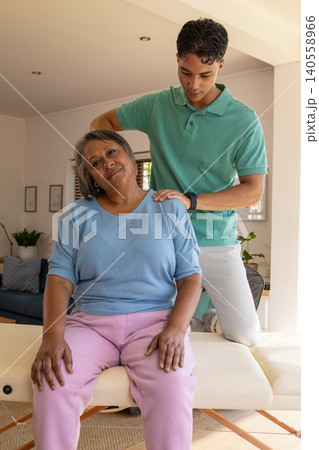 Senior woman receiving shoulder massage from male caregiver on therapy table in living room Senior woman receiving shoulder massage from male caregiver on therapy table in living room 140558966