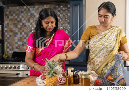 Indian mother with daughter in sarees sorting fresh produce on kitchen island with reusable bags Indian mother with daughter in sarees sorting fresh produce on kitchen island with reusable bags 140558999