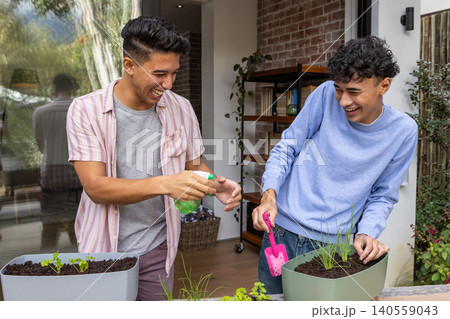 Diverse male friends gardening on deck table planting seedlings with spray bottle, trowel Diverse male friends gardening on deck table planting seedlings with spray bottle, trowel 140559043