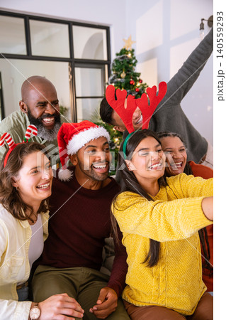Diverse friends leaning in on sofa at home under christmas tree taking selfie with smartphone Diverse friends leaning in on sofa at home under christmas tree taking selfie with smartphone 140559293