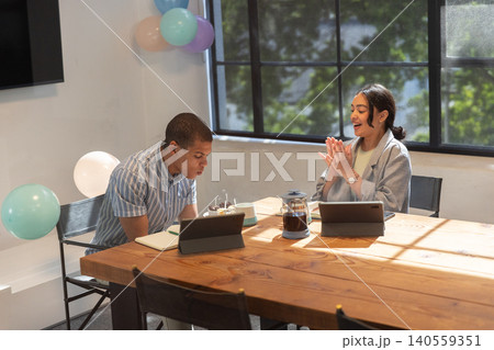 Diverse colleagues celebrating birthday at office table, tablets, cake, french press, balloons Diverse colleagues celebrating birthday at office table, tablets, cake, french press, balloons 140559351