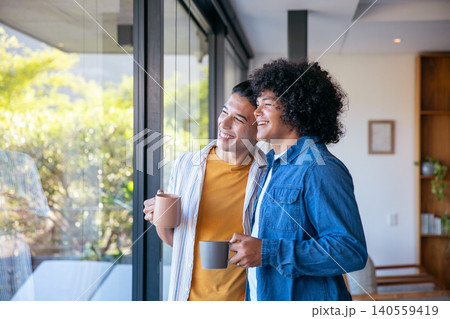 Two men holding ceramic mugs and gazing through floor-to-ceiling glass door in modern living room 140559419