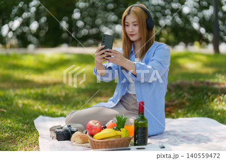 Asian woman enjoying spring outdoor picnic, creating social media content with smartphone Asian woman enjoying spring outdoor picnic, creating social media content with smartphone 140559472