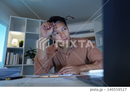 Asian man in his 20s working late at home office feeling stressed Asian man in his 20s working late at home office feeling stressed 140559527