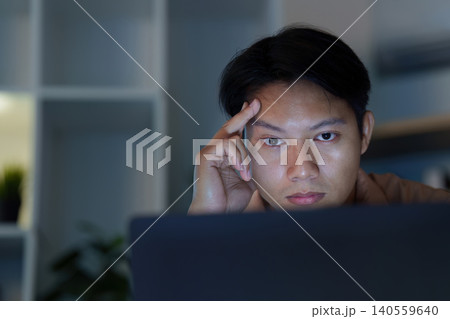 Asian man stressed working on laptop at home office desk late night Asian man stressed working on laptop at home office desk late night 140559640