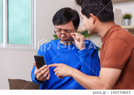 Asian senior man learning smartphone with young man helping at home 140559663