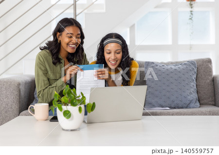 Diverse mom and teenage daughter reviewing letter from blue envelope on sofa at home 140559757