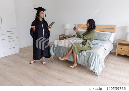 Diverse mother recording teenage daughter in gown giving speech in bedroom Diverse mother recording teenage daughter in gown giving speech in bedroom 140559786