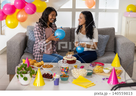 Diverse mom and teenage daughter preparing blue balloons and arranging cake candles on table Diverse mom and teenage daughter preparing blue balloons and arranging cake candles on table 140559813