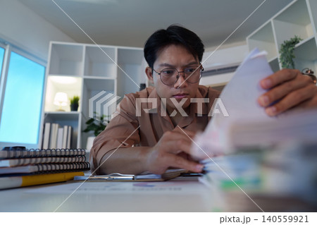 Asian man in his 20s working late at home office with documents Asian man in his 20s working late at home office with documents 140559921
