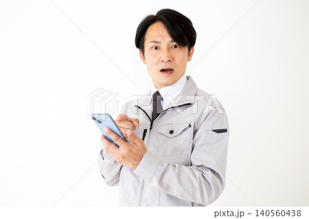 スマホを見てショックを受けるグレーの作業着のミドル男性ビジネスマン白バック 140560438