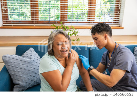 Senior woman wincing while asian healthcare provider using syringe on sofa in room Senior woman wincing while asian healthcare provider using syringe on sofa in room 140560553