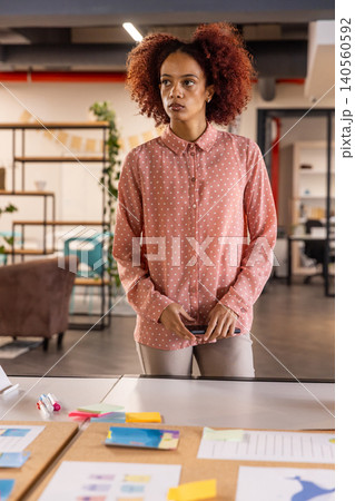 African american woman holding smartphone and sorting project papers at office desk African american woman holding smartphone and sorting project papers at office desk 140560592