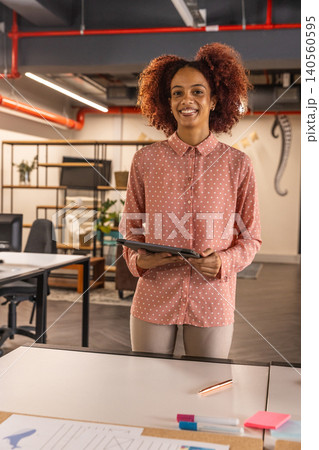 African american woman at white desk with tablet and glancing at computer monitors in office 140560595