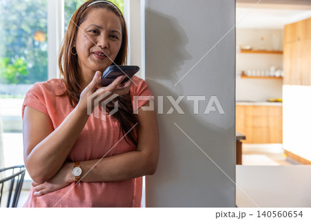 Asian woman leaning at home by cabinets, window checking smartphone, wristwatch Asian woman leaning at home by cabinets, window checking smartphone, wristwatch 140560654